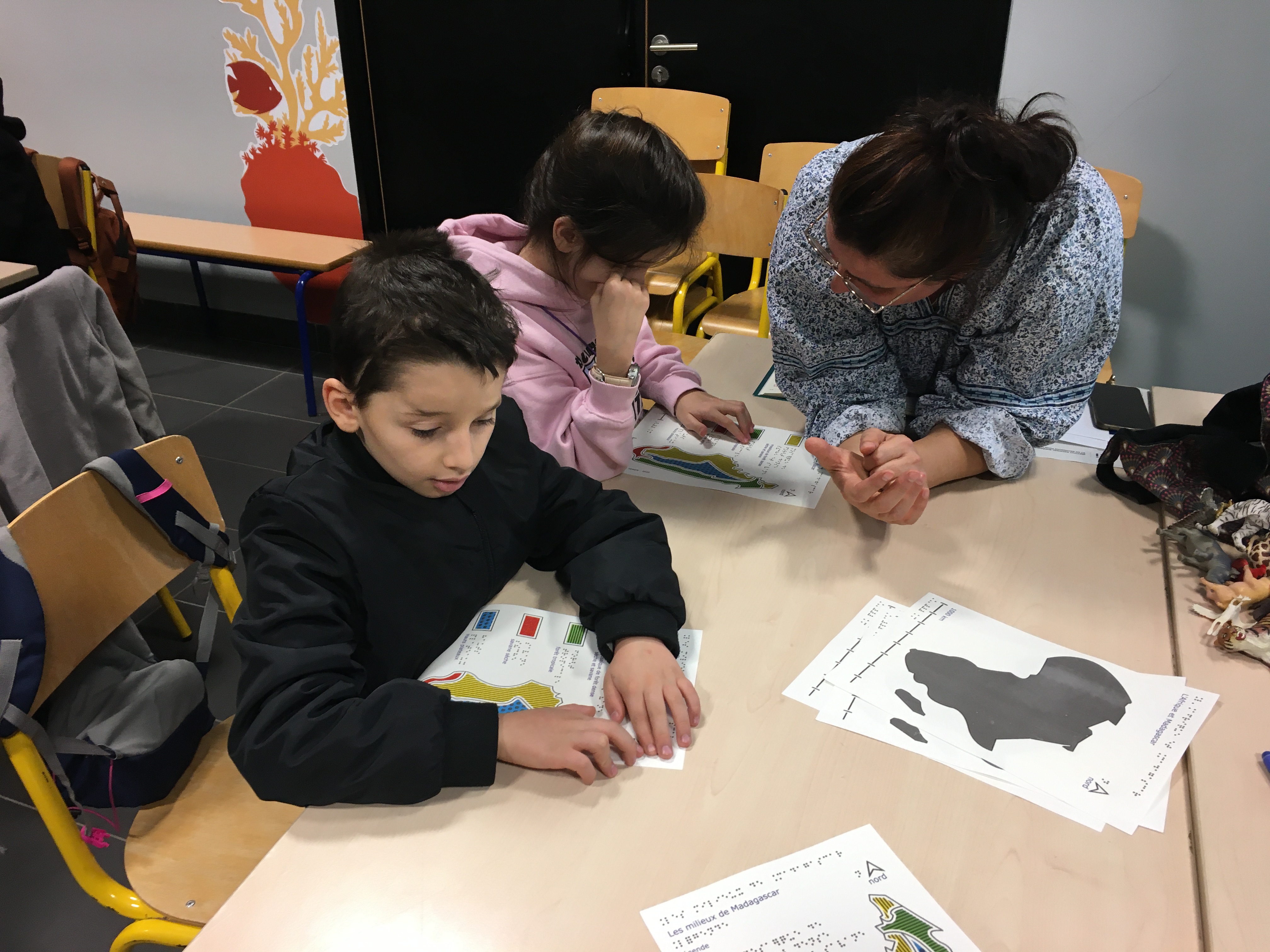 Deux élèves et leur enseignante explorant la carte des milieux de Madagascar