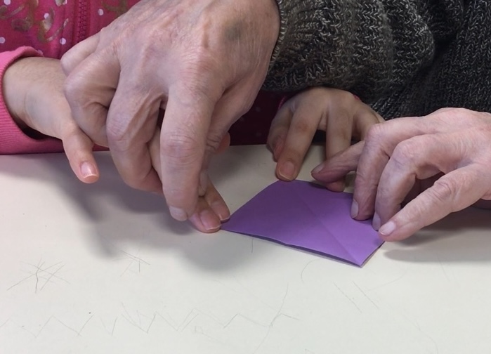 Une élève se fait aider pour plier un carré de papier