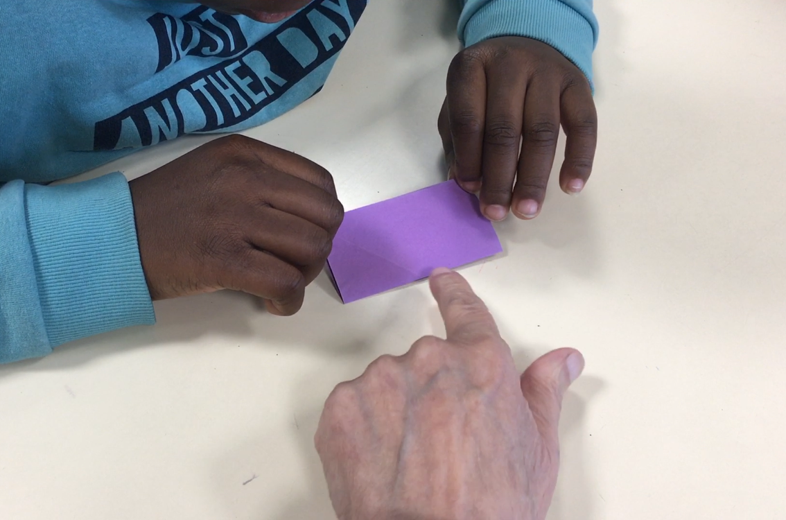 Une élève se fait aider pour plier un carré de papier